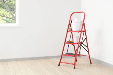 Beyaz duvarın yanında boya ve fırça dolu merdiven.