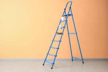 Turuncu duvarın yanında boya ve aletlerle dolu bir merdiven.