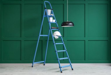 Yeşil duvarın yanında boya ve fırça dolu merdivenler.