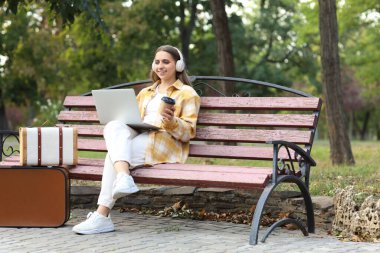 Kulaklıklı ve kahveli bayan turist sonbahar günü bilgisayarı park halinde kullanıyor.