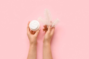 Kozmetik krem kavanozu ve pembe arka planda Noel ağacı dalıyla kadın elleri