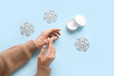 Mavi arka planda kar taneleri olan kozmetik krem süren bir kadın