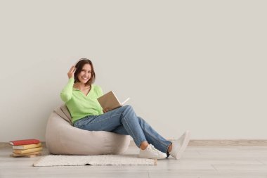 Kulaklıklı güzel bir bayan evde puf minderiyle kitap okuyor.