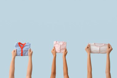 Mavi arka planda bebek kıyafetleri olan kadın elleri.