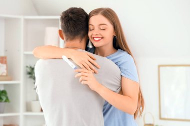 Hamilelik testi olan mutlu genç çift yatak odasında sarılıyor.