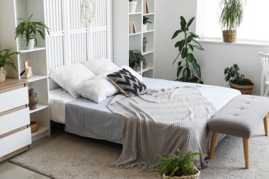 Yatak odasının içinde rahat bir yatak, raflar ve ev bitkileri var.