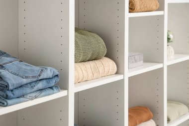 Aydınlık duvarın yanında farklı kıyafetleri olan raf ünitesi, yakın çekim.