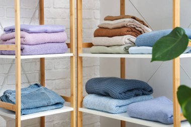 Hafif tuğla duvarın yanında katlanmış giysileri olan raf ünitesi.