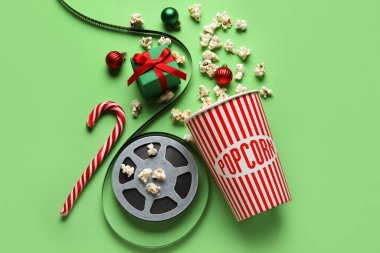 Bir kova patlamış mısır, film makarası, hediye kutusu ve yeşil arka planda Noel dekoru.