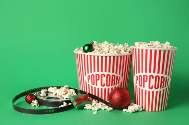 Patlamış mısır, film makarası, hediye kutusu ve yeşil arka planda Noel topları.