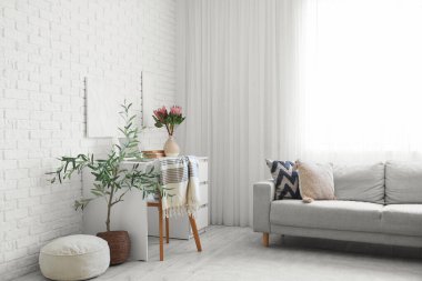 Oturma odasının içinde kanepe, işyeri ve vazoda protea çiçekleri var.