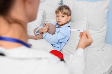 Suçiçeği hastası küçük bir çocuk ve yatak odasında termometre tutan bir doktor.