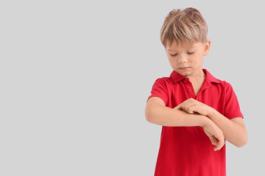 Little boy ill with chickenpox scratching his arm on light background clipart