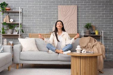 Evdeki kanepede meditasyon yapan güzel genç bir kadın.