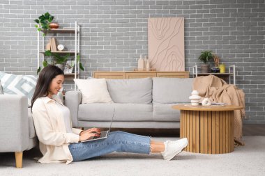 Evdeki halıda dizüstü bilgisayar kullanan güzel bir kadın.