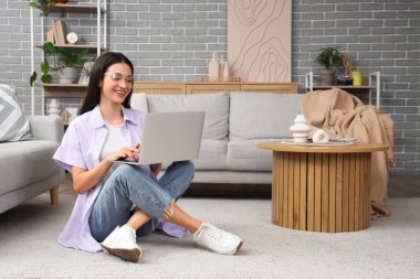 Evdeki halıda dizüstü bilgisayar kullanan güzel bir kadın.