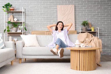 Evdeki gri kanepede dinlenen güzel genç bir kadın.