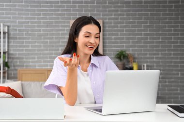 Evdeki masada dizüstü bilgisayarla görüntülü sohbet eden güzel bir kadın.