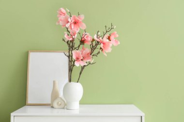 Manolya çiçekli vazo ve yeşil duvarın yanındaki klozette.