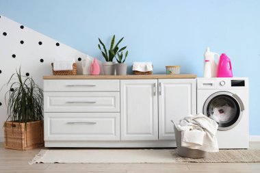 Çamaşır makinesi, deterjan ve sepeti olan çamaşır odasının içi.