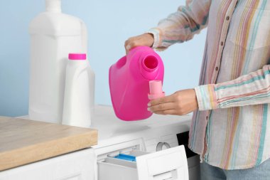 Çamaşır makinesinin yanına çamaşır deterjanı döken kadın.