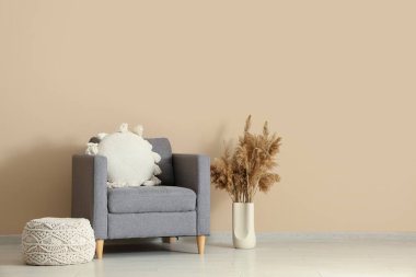 Yastıklı koltuk, vazoda otlar ve odada bej duvarın yanında puf.