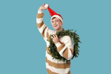 Mavi arka planda Noel çelengi olan genç adam.