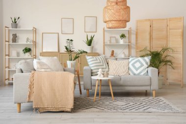 Gri kanepeler, raf üniteleri ve bitkilerle aydınlık oturma odasının içinde.