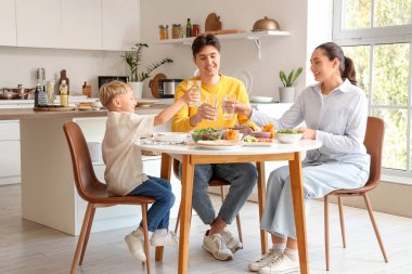 Küçük çocuk ve ailesi bir bardak suyla mutfakta Fajita yiyorlar.