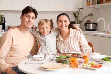 Ebeveynler ve küçük oğulları mutfakta lezzetli Fajita ile masada kucaklaşıyorlar.