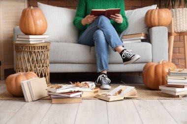 Kanepede kitap okuyan bir kadın balkabağı ve sonbahar yapraklarıyla evde.