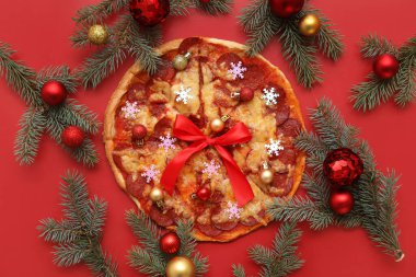 Lezzetli pizza dilimleri, köknar dalları ve kırmızı arka planda Noel dekoru olan kompozisyon