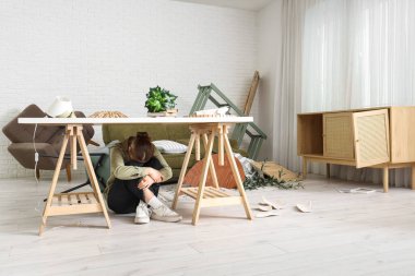 Depremden sonra dağınık oturma odasında masanın altında saklanan genç bir kadın.