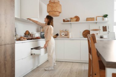 Mutfakta çekmecesi açık, dolabı açık genç bir kadın.