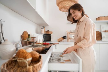 Genç bir kadın mutfaktaki çekmeceden çırpı alıyor.