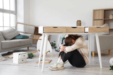 Deprem sırasında dağınık oturma odasında masanın altında saklanan genç bir kadın.