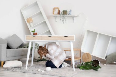 Deprem sırasında evdeki masanın altında saklanan korkmuş kadın.