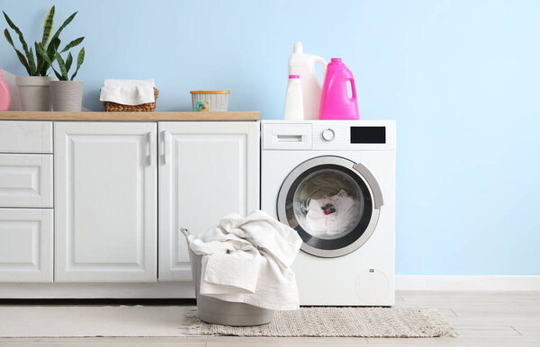 Интерьер прачечной со стиральной машиной, моющими средствами и корзиной