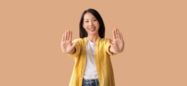 Genç Asyalı kadın bej arka planda el sallıyor.