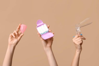 Regl bardağı, tampon ve bej arka planda jinekolojik spekulum olan eller.