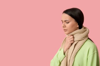 Pembe arka planda boğazı ağrıyan fularlı güzel bir kadın.