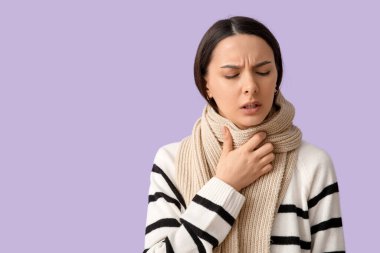 Eşarplı güzel bir kadın leylak arka planında boğaz ağrısı çekiyor.