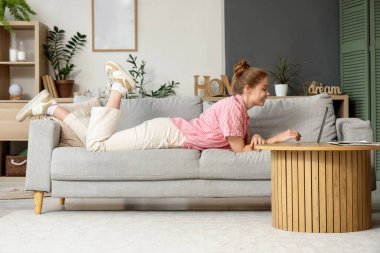 Evdeki koltukta modern laptop kullanan genç bir kadın.