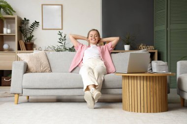 Modern dizüstü bilgisayarlı genç bir kadın evdeki kanepede dinleniyor.