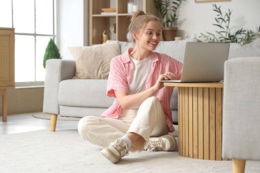 Evdeki masada modern laptop kullanan genç bir kadın.