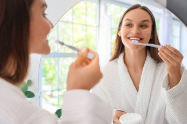 Banyoda aynanın yanında dişlerini pudralayan genç bir kadın.