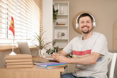 Evde internetten İspanyolca öğrenen kulaklıklı yakışıklı bir adam.