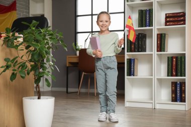 Evde İspanyol bayrağı ve kitabı olan küçük bir kız.