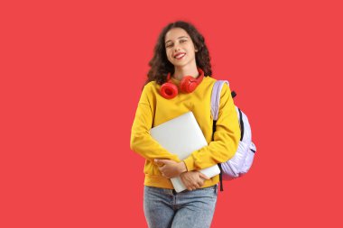 Kırmızı arka planda dizüstü bilgisayarı olan kız öğrenci.