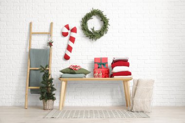 Kış elbiseli bank, Noel dekoru, merdiven ve yastıklar beyaz tuğla duvarın yanında sepette.
